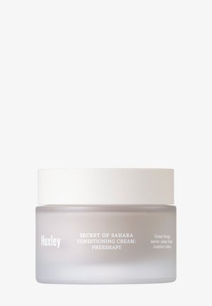 Huxley Geheimnis der Sahara Pflegecreme in einem zylindrischen, frosted Glasbehälter mit einem weißen Deckel. In Weiß gedruckter Text beinhaltet Produktnamen und Slogan.