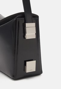 Sac en cuir verni noir avec une forme structurée, présentant un accent de verrou carré en argent et une bandoulière en cuir lisse.