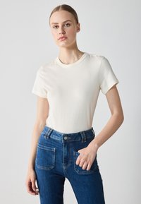 White short-sleeve t-shirt in soft fabric paired with high-waisted blue jeans featuring visible stitching and two back pockets.