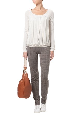 Lys beige langærmet top med plisseringer og udsmykning, parret med grå leggings med trykt tekst, mens hun holder en brun lædertaske.