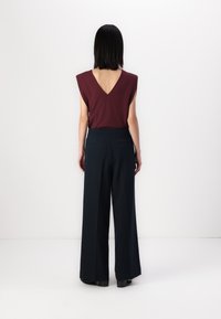 Maroon V-neck top with cap sleeves, paired with navy wide-leg trousers. Smooth fabric with a structured silhouette and discreet back pockets.