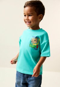 Türkisfarbenes Baumwoll-T-Shirt mit kurzen Ärmeln, versehen mit einer verspielten Grafik eines Löwen, eines Krokodils und dem Text "Safari Fun" in kräftigen Farben.