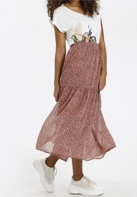 Falda midi rosa y fluida con un patrón de estampado de leopardo negro, combinada con una camiseta blanca de manga corta con un diseño botánico, y zapatillas blancas.