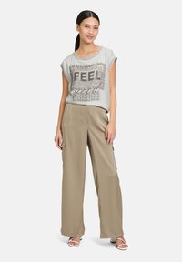 Haut gris clair à manches courtes avec un imprimé "FEEL", associé à un pantalon beige à jambes larges. Tissu lisse, coupe décontractée, design minimaliste.