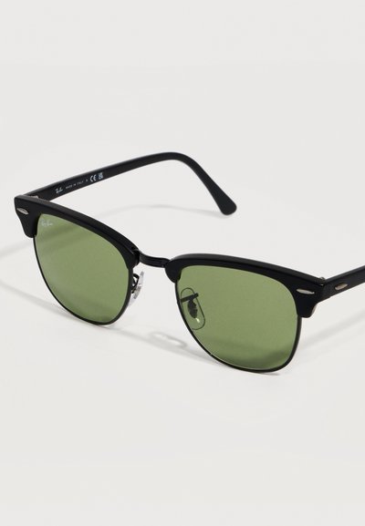Черни рамки на слънчеви очила Ray-Ban с зелени нюанси на стъклата и класически дизайн Clubmaster на обикновен светъл фон.