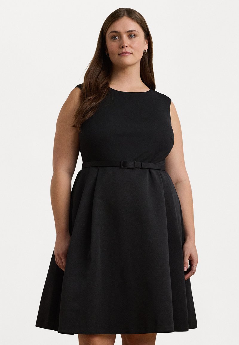 Svart ärmlös klänning med figurnära överdel och utsvängd kjol, med bälte i midjan. Slät textur och klassisk silhuett.