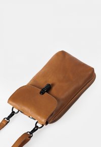 Braune Leder-Handytasche mit Frontklappe, schwarzem Verschluss, Reißverschluss an der Seite und zwei abnehmbaren Riemen mit schwarzen Metallklammern.