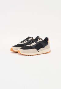 Schwarze und beige Sneakers mit Netzpaneelen, runder Zehenpartie, Schnürverschluss und Gummisohle. Mit orangefarbenen Akzenten an der Ferse und Sohle.