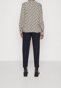 Patterned blouse in cream and black with a geometric design, paired with navy trousers and black heeled boots. Long sleeves, relaxed fit.