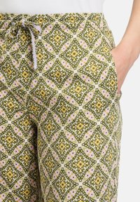 Patroonbroeken met een groen en geel geometrisch ontwerp op een lichte achtergrond, met een elastische tailleband en zijzakken.