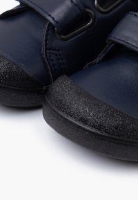Navy blue leather shoes with Velcro straps, featuring a textured black rubber sole. Rounded toe design with stitching details.
