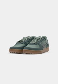 Green sneakers with a combination of smooth and textured fabric, featuring a thick gum sole and subtle branding on the side.