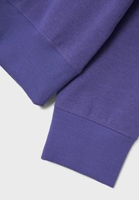 Tessuto della felpa viola con polsini a coste e dettagli di trama sottili. Presenta una superficie liscia ed è visivamente uniforme nel colore.