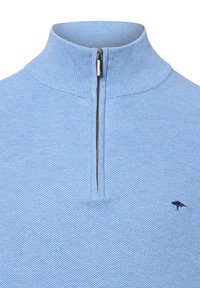 Jasnoniebieski pulower z wysokim kołnierzem, półzbliżeniowym zapięciem i teksturowanym wzorem dzianiny. Posiada mały ciemny emblemat z boku.