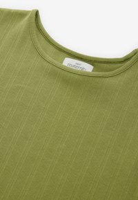 Groen zwangerschapshemd met een geribbelde textuur, ronde halslijn en label met "NEXT maternity." Getailleerd ontwerp met eenvoudige stiksel details.