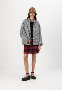 Veste oversize en sequins argentés, top ajusté noir, jupe à carreaux rouge et chaussures noires à semelle épaisse. Un chapeau seau à motifs marron complète le look.