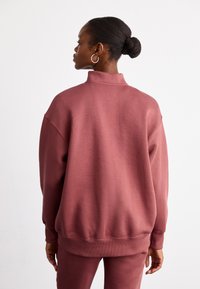 Sweatshirt granada de tamanho grande com gola alta, feito de material macio, com ombros caídos e punhos canelados. Design simples sem padrões.