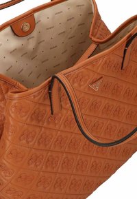 Borsa a tracolla marrone trapuntata realizzata in pelle sintetica. Presenta motivi floreali in rilievo, bordi neri e un rivestimento interno beige con monogramma.
