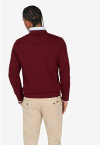 Maglione testurizzato bordeaux con scollo tondo, polsini e orlo a costine, abbinato a pantaloni beige con tasche posteriori e dettagli con bottoni.