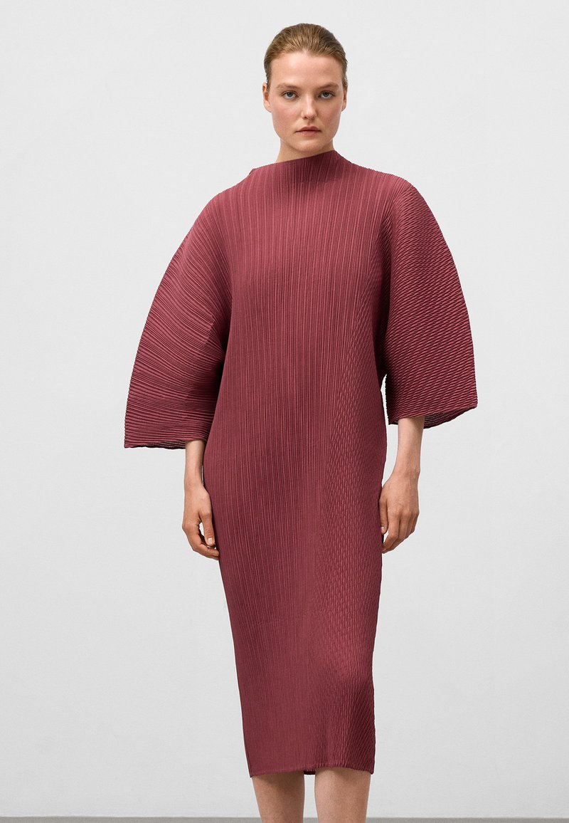 Bordeauxfarbenes plissiertes Kleid mit einem hohen Halsauschnitt und weiten Ärmeln, das eine vertikale Rippstruktur aufweist und bis zur Mitte der Wade reicht.