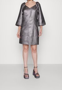 Metallinhohtoinen hopeanvärinen minimekko, jossa teksturoitu kangas, V-pääntie, puhvimaiset hihat ja suora leikkaus. Yhdistetty paksukorkoisiin sandaaleihin.