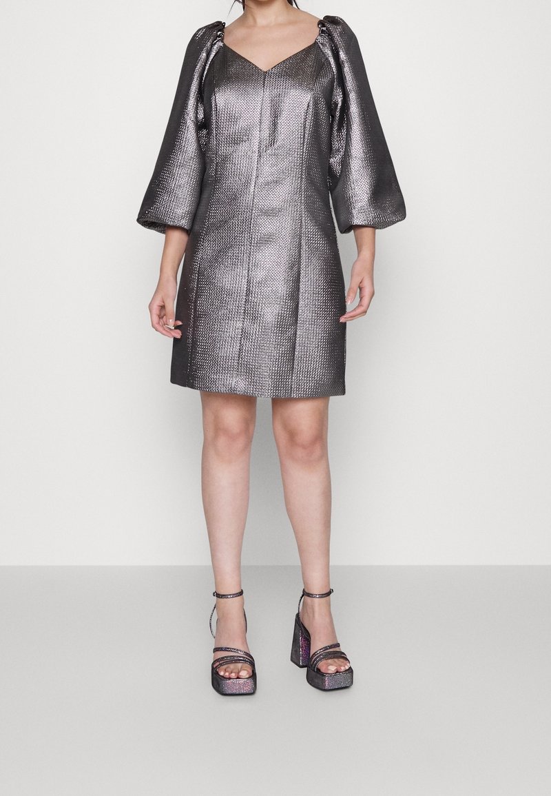 Metallinhohtoinen hopeanvärinen minimekko, jossa teksturoitu kangas, V-pääntie, puhvimaiset hihat ja suora leikkaus. Yhdistetty paksukorkoisiin sandaaleihin.