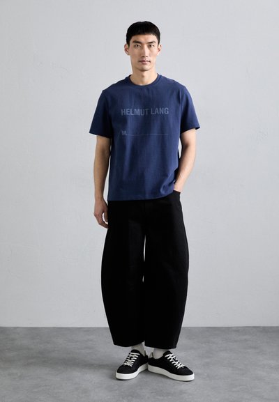Mørkeblå bomull t-skjorte med "HELMUT LANG" tekst, kombinert med svarte vide bukser og svarte sneakers med hvite såler og snører.