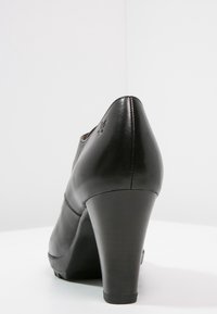 Chaussure à talon haut en cuir noir avec une finition brillante, un bout arrondi et un talon solide. Présente des détails de couture subtils le long de la tige.