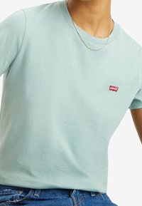 Světlá mátově zelená bavlněná tričko s kulatým výstřihem a krátkými rukávy, se malou červenou nášivkou loga Levi's na levé části hrudi.