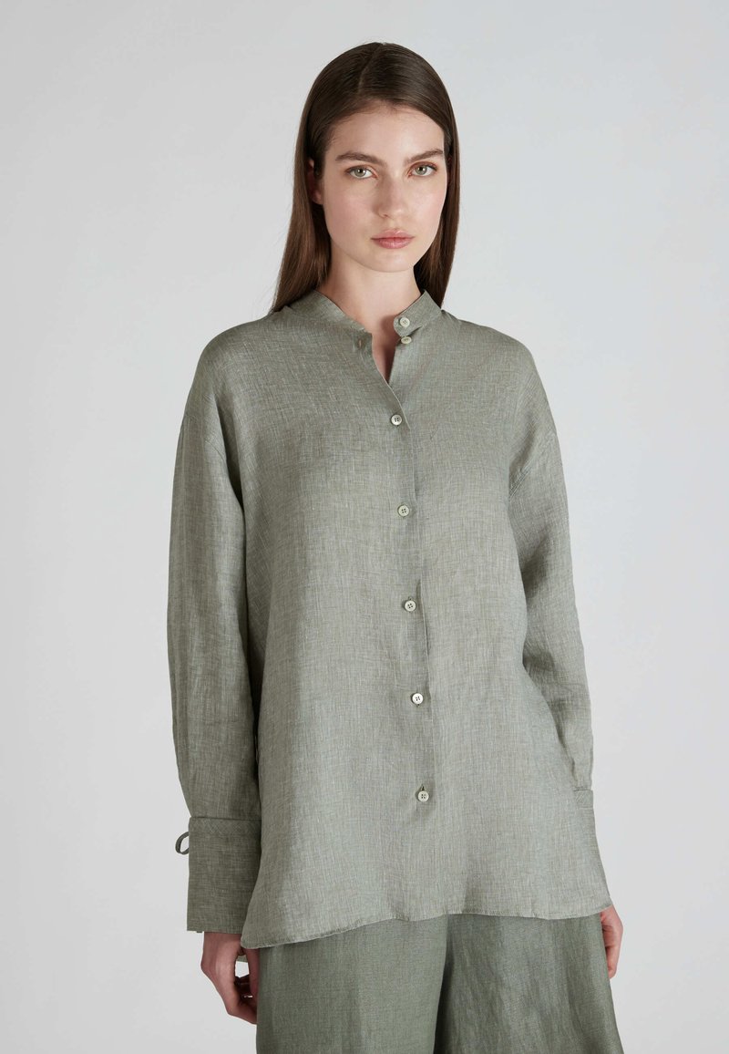 Camicia di lino verde chiaro con un design senza colletto, chiusura a bottoni, maniche lunghe e una vestibilità leggermente larga. Texture sottile e morbido cadere.
