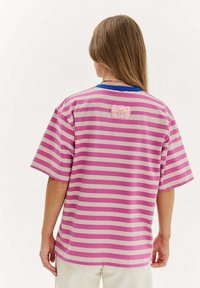 Růžovo-šedý pruhovaný tričko s modrým límečkem. Na zadní straně je čtvercová nášivka s květinovým vzorem. Krátké, volné rukávy.