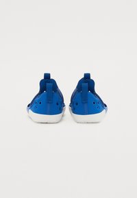 Blå slip-on sko med nettdetaljer, fleksibel såle, polstret hæl og bakre trekkhank. Har ventilasjonshull for pusteevne.