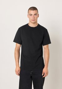 Schwarzes Baumwoll-T-Shirt mit kurzen Ärmeln, Rundhalsausschnitt und schlichtem Design. Kombiniert mit dunkelblauer Denim-Jeans mit lockerem Schnitt.