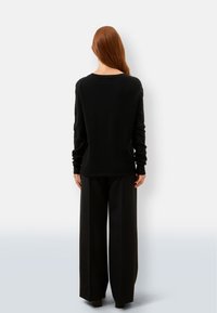 Schwarzer Pullover mit langen Ärmeln, Rundhalsausschnitt und gerippten Bündchen. Kombiniert mit weit geschnittenen schwarzen Hosen, glatte Textur, minimalistisches Design.