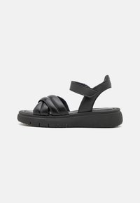 Sandales en cuir noir avec un design de bande tressée, une sangle de cheville réglable et une semelle rembourrée pour le confort. Semelle extérieure en caoutchouc texturé.