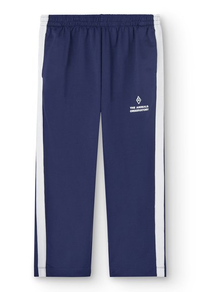 Marinblå träningbyxor med vita sidostickningar, elastisk midja och logotyp broderad på vänster lår. Slät tyg, avsmalnande design.
