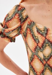 Robe à motifs avec des manches bouffantes dans des teintes chaudes d'orange, de vert et de beige ; le tissu a une apparence texturée et légère.
