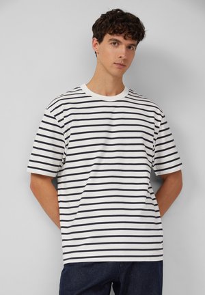 T-shirt blanc à manches courtes avec des rayures horizontales bleu marine, col rond et coupe décontractée, associé à un jean noir.