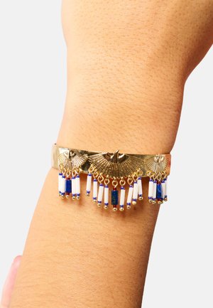 Bracelet jonc en ton or avec un design en forme de éventail, agrémenté d'accents de perles bleues et blanches, et d'éléments pendants pour plus de détails.