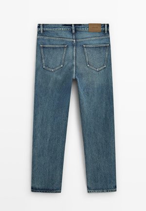 Blaue Jeans aus Denim zeichnen sich durch ein gerades Bein Design, hintere Taschen mit winkligen Formen und ein braunes Etikett über dem Bund aus.