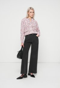 Mnohobarevný pletený svetr s límečkem, doplněný vysokými černými kalhotami s širokými nohavicemi a černými lodičkami. Doplňky zahrnují černou tašku.