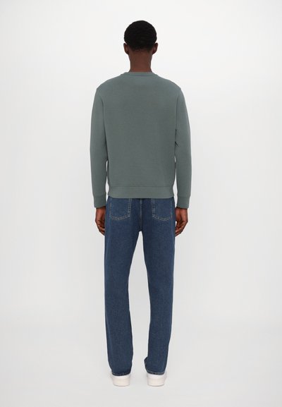 Sudadera verde con cuello redondo, mostrada desde la parte de atrás. Combinada con jeans de mezclilla azul holgados y zapatillas blancas. Textura y diseño simples.
