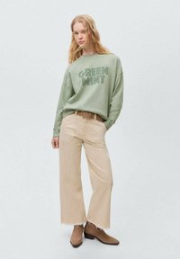 Mintgroene sweatshirt met de tekst "GREEN MINT", gecombineerd met lichtbeige wijde broek met rafelige hems en bruine laarzen.