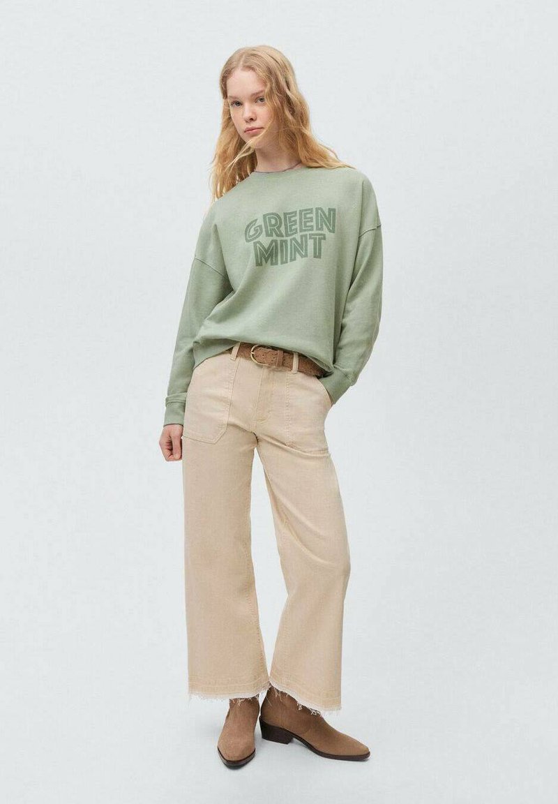 Mintgroene sweatshirt met de tekst "GREEN MINT", gecombineerd met lichtbeige wijde broek met rafelige hems en bruine laarzen.