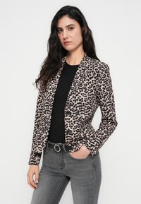 Σακάκι με λεοπάρ σχέδιο σε απαλό ύφασμα, με γιακά με εγκοπή, κούμπωμα με ένα κουμπί και δύο μπροστινές τσέπες. Φορεμένο πάνω από μαύρο τοπ.
