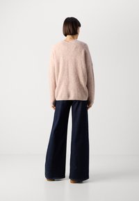 Helles rosa, übergroßes Sweatshirt mit einer weichen Textur, kombiniert mit dunkelblauen weit geschnittenen Jeans. Minimalistisches Design mit einem runden Ausschnitt.