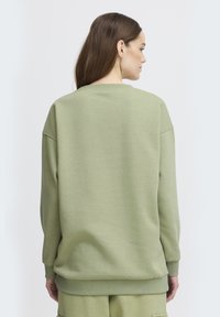 Felpa verde con una vestibilità rilassata, polsini e orlo ribattuti, texture morbida e design a girocollo. Cuciture visibili sulle spalle e sulla schiena.