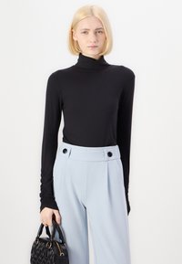 Un turtleneck noir à manches longues avec une texture côtelée, associé à un pantalon large taille haute bleu clair avec des boutons noirs ; tenant un sac noir.