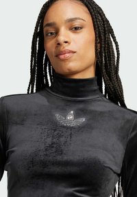 Svart sammetstopp med hög hals och en logotyp prydd med kristaller på bröstet. Slät textur med figursydd design och långa ärmar.