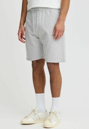 Pantaloni corti in misto cotone grigi con vita elastica e cordino, dotati di tasche laterali e vestibilità ampia. Abbinati a sneakers bianche e calzini.